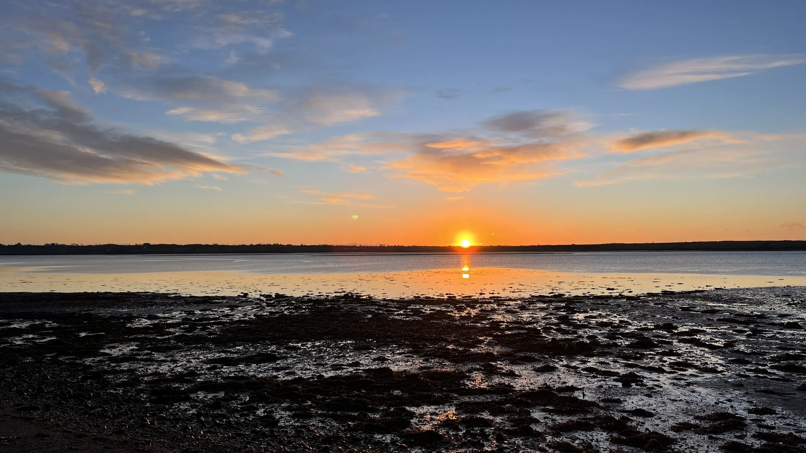 The sun setting over Bannow Bay, the sky washed orange and gold above the dark far shore and the wet sand catching the light.