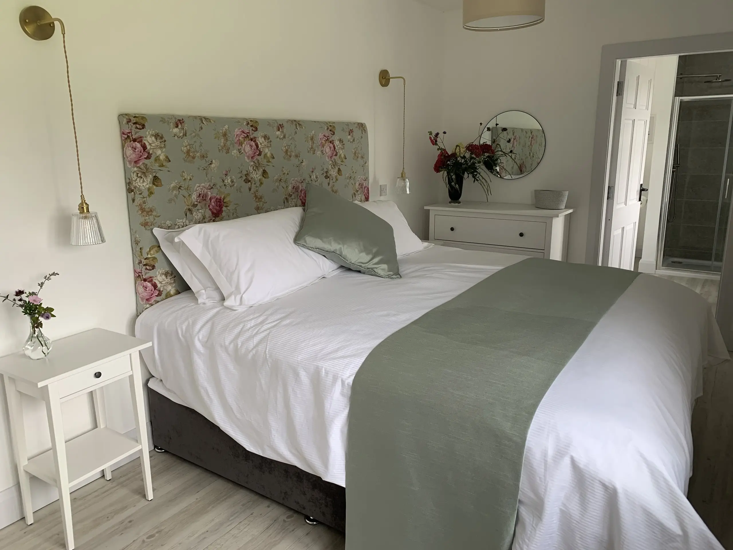 The Paddock Bedroom: a super-king bed with a floral headboard, sage green runner and a round mirror above the drawers.