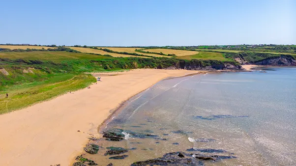 Booley Bay: a long sweep of golden sand curving into a sheltered bay, backed by green farmland running down to the shore.