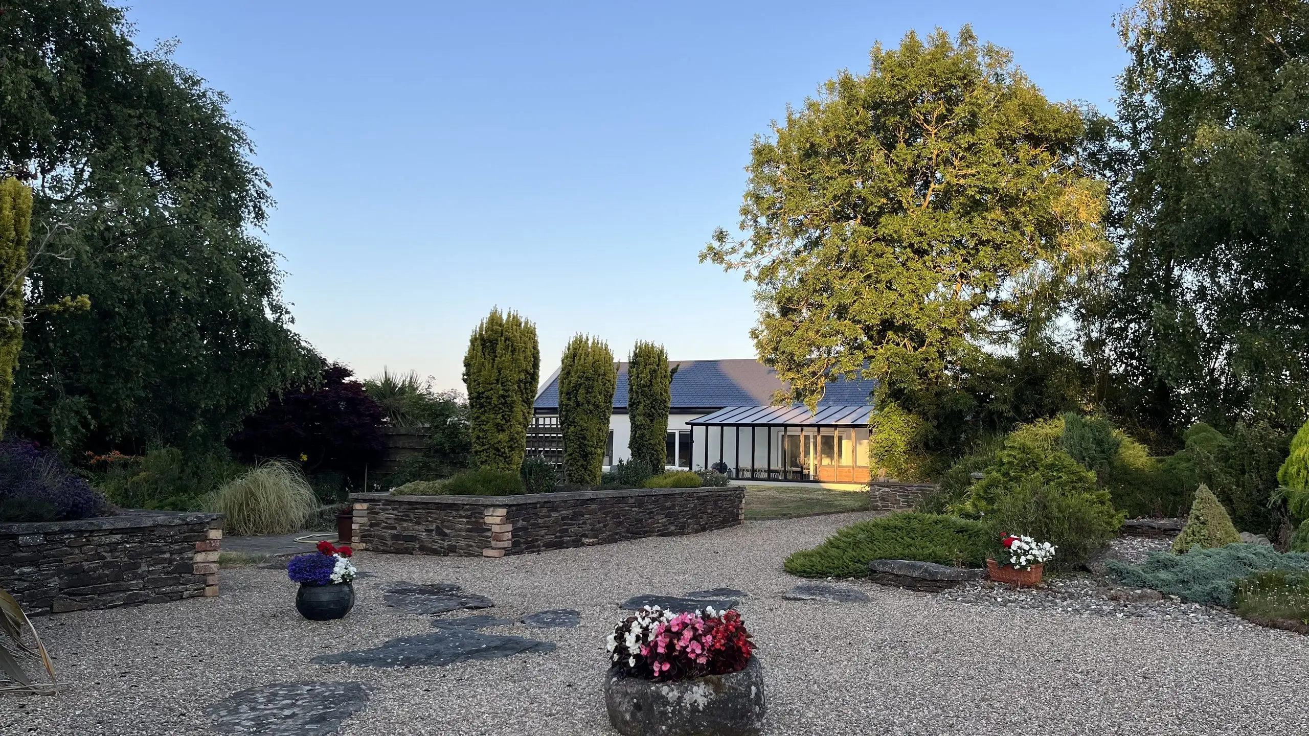 The cottage across the garden at golden hour, a gravel path winding between planted borders to the veranda.