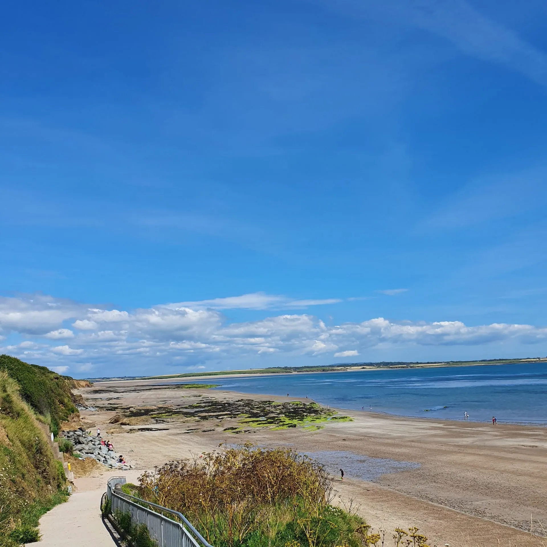 Grange beach: a long sweep of sand curving around a shallow bay under a big cloudy sky.