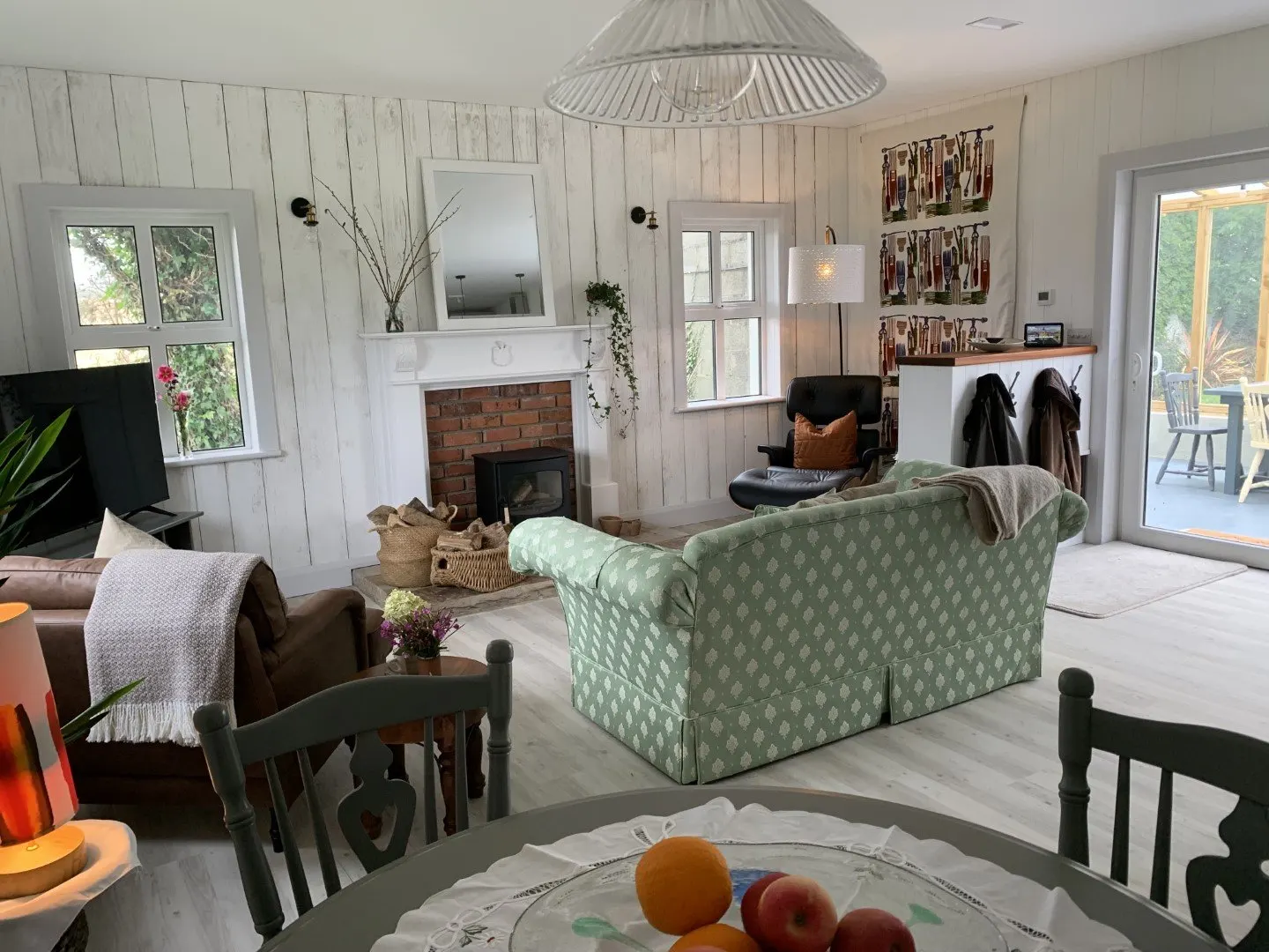 The open-plan living area with a green sofa, dining table and a fireplace, opening onto the garden.