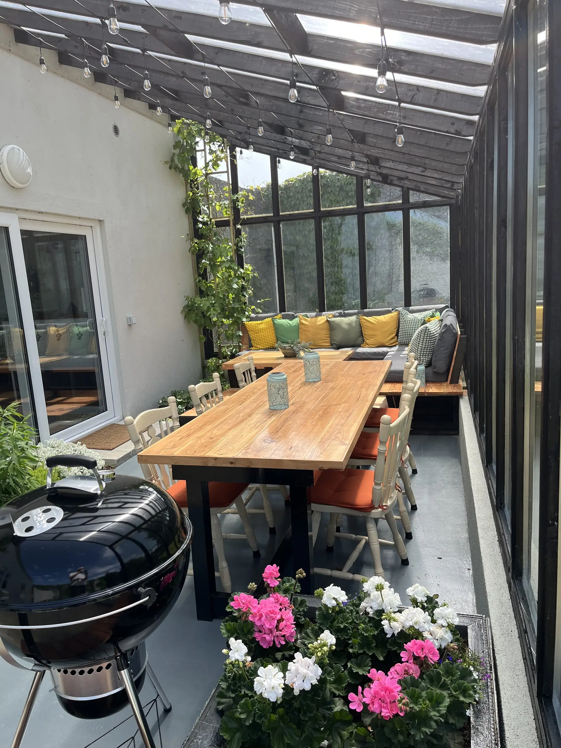 The length of the glazed porch from the far end, the dining table and bench seating with the garden beyond.